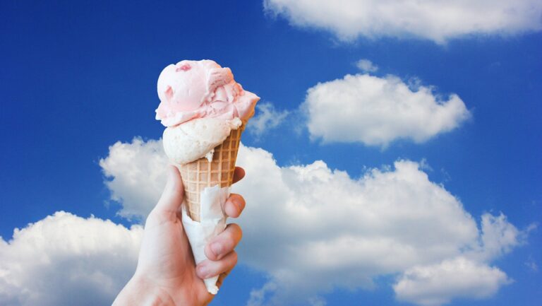 Eine Hand hält ein Eis, im Hintergrund hellblauer Himmel.